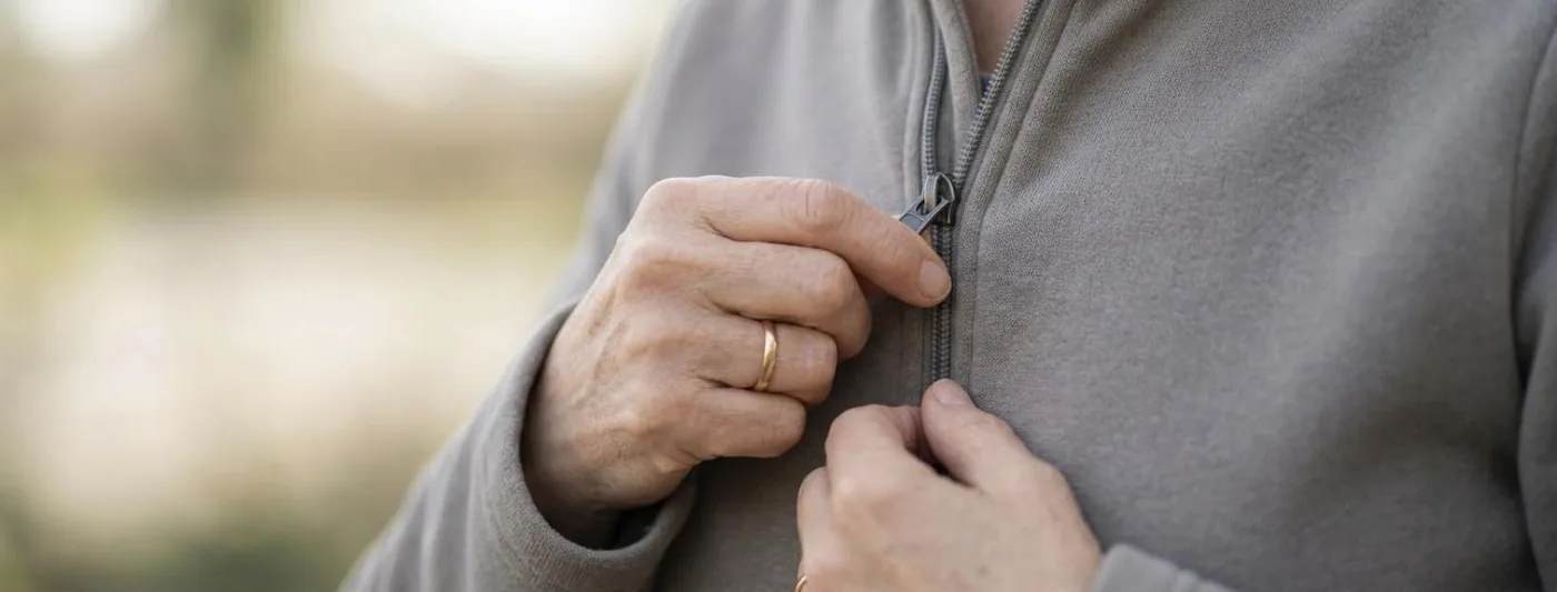Feinmotorik üben: Eine Hand zieht den Schieber eines Reissverschlusses nach oben, die andere hält den Stoff fest (Symbolbild, mit künstlicher Intelligenz erzeugt)